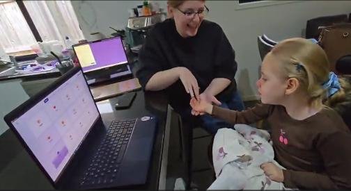 A child using AshySpeak on a laptop with a carer beside her